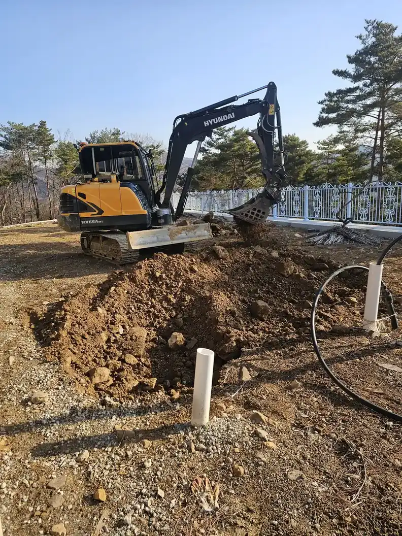 굴착기로 판 구덩이 옆에 흰색 배관 두 개가 지면 밖으로 나온 배관 매립 작업 시공 전