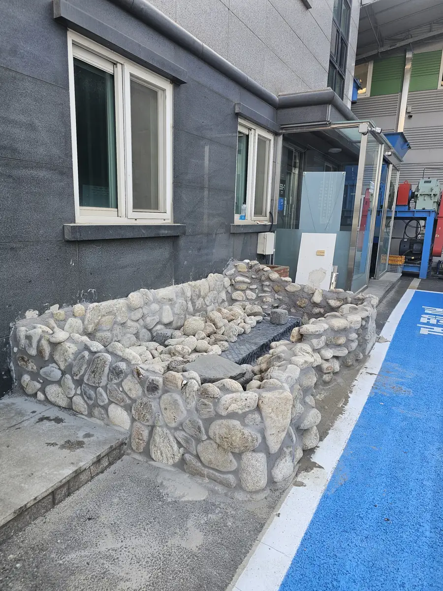 푸른 바닥 구획선 옆에 놓인 석축 수조를 측면에서 본 모습 진행 중